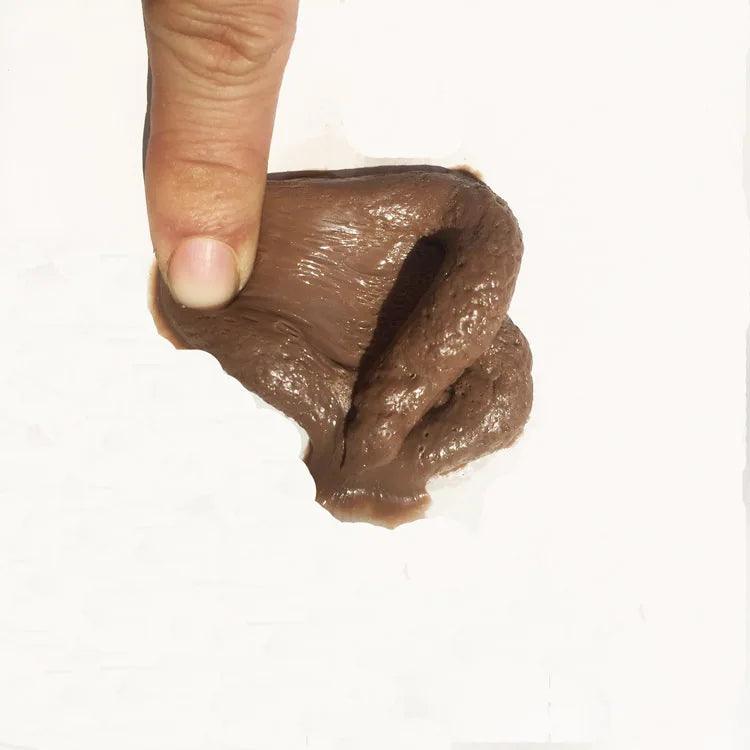 Realistic fake poop being stretched by a hand, showing its flexible texture on a white background.
