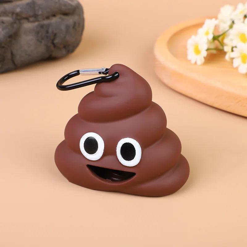 Brown poop emoji bag with a carabiner clip, featuring a happy face, placed on a beige surface with flowers.
