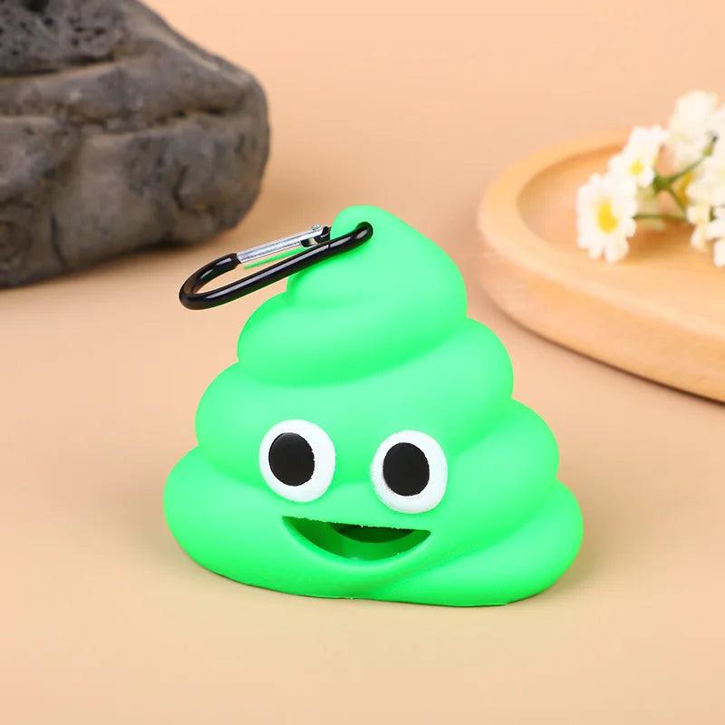 Green poop emoji bag with a carabiner clip, featuring a happy face, on a beige surface with flowers in the background.