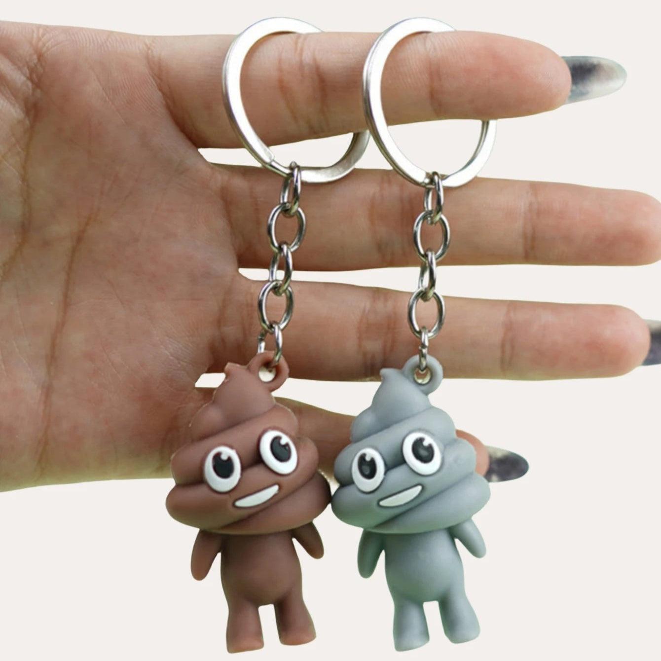 Hand holding brown and gray poop emoji keychains with happy faces on metal keyrings.