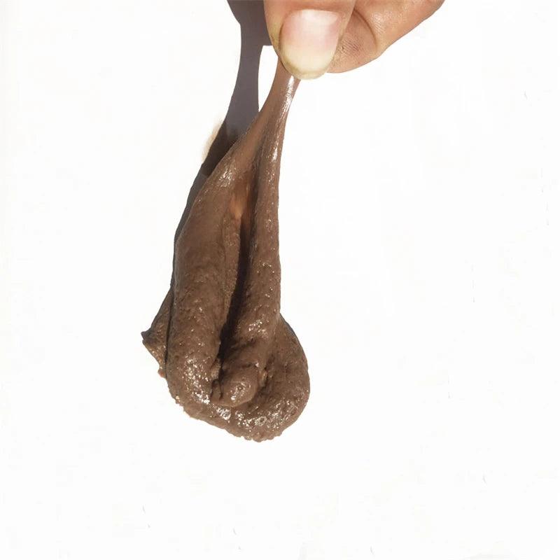 Realistic fake poop with a hand lifting it, showing its texture and shape on a white background.