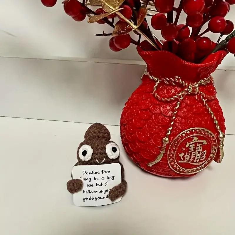 Positive Poop plush next to a red vase with berries, holding an uplifting sign.