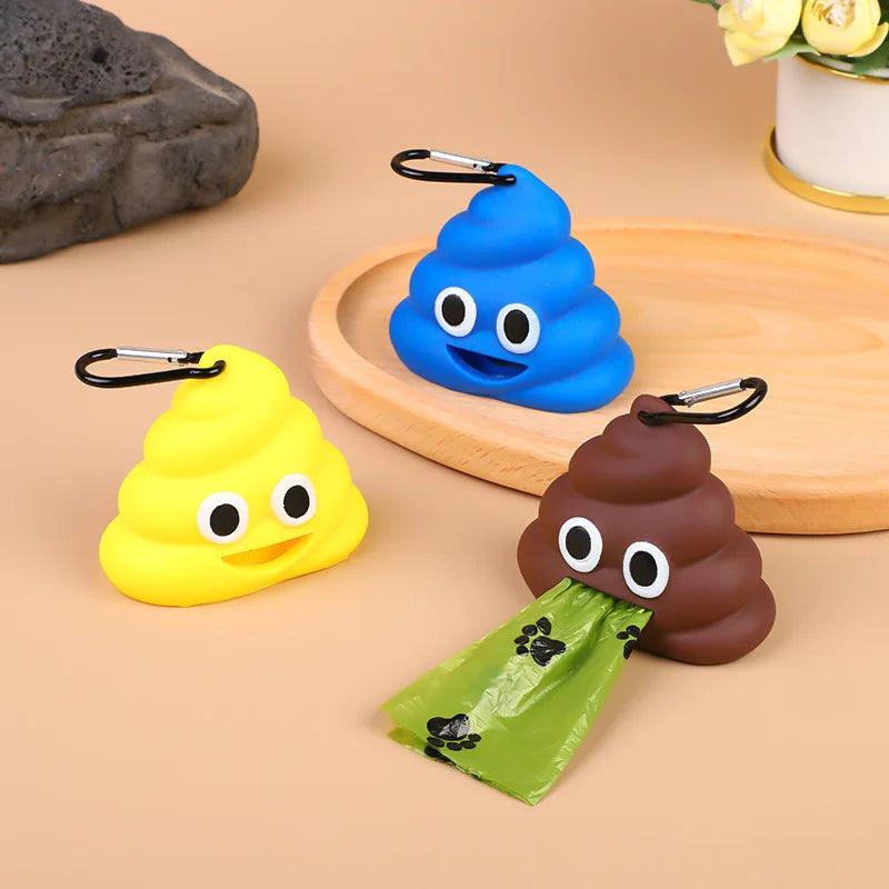 Blue, yellow, and brown poop emoji poop bag dispensers with a green bag pulled out, on a wooden tray with flowers.