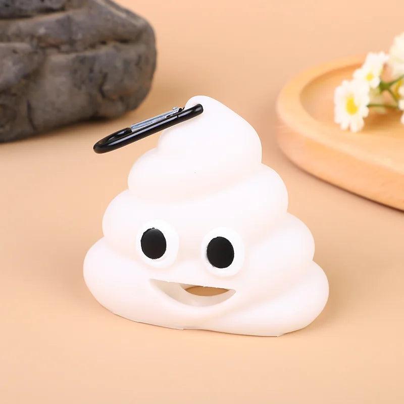 White poop emoji bag with a carabiner clip, showing a happy face, on a beige surface with a wooden tray and flowers.